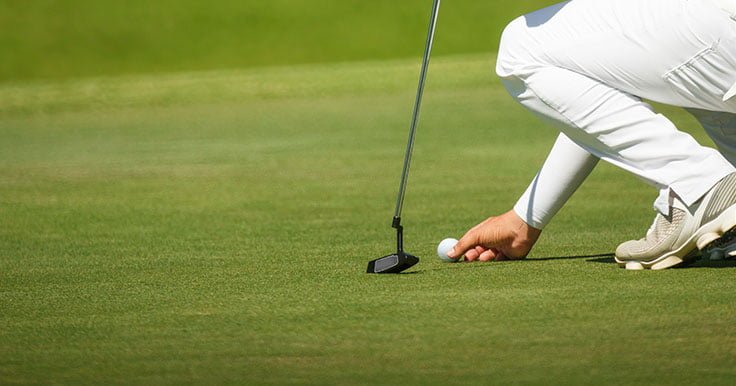 A golfer is placing a golf ball marker on the green.